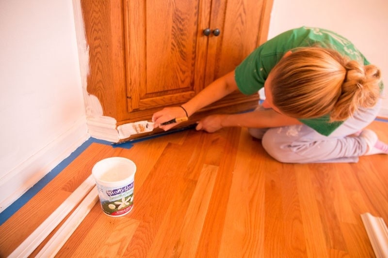 how to paint baseboards- woman painting baseboards white