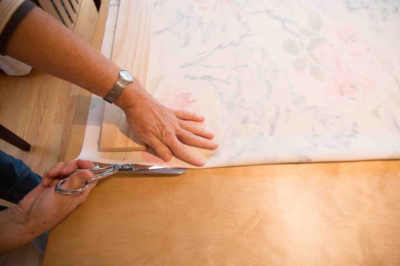 woman making roman shades by cutting fabric with fabric shears