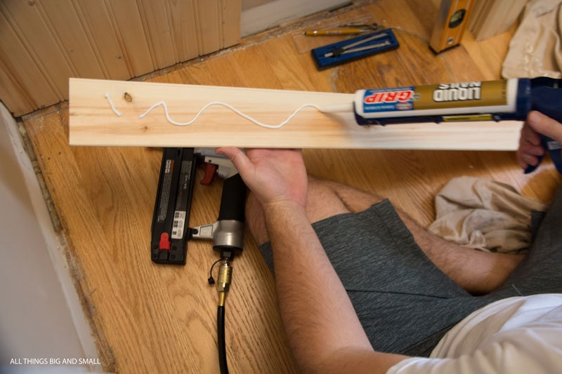 applying liquid nails wood glue to the back of beadboard planks in beadboard bathroom