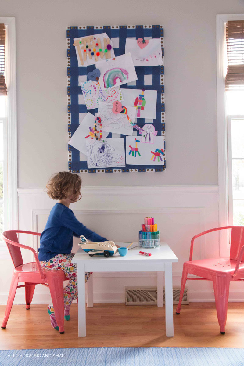 girl drawing at table below fabric covered bulletin board