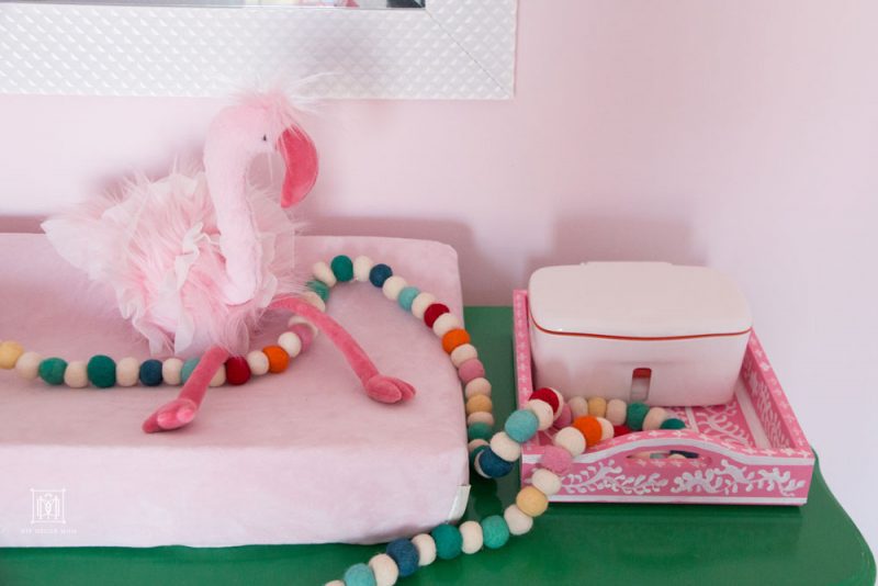 pink flamingo stuffed animal on top of pink changing mat on green dresser in pink girls shared bedroom