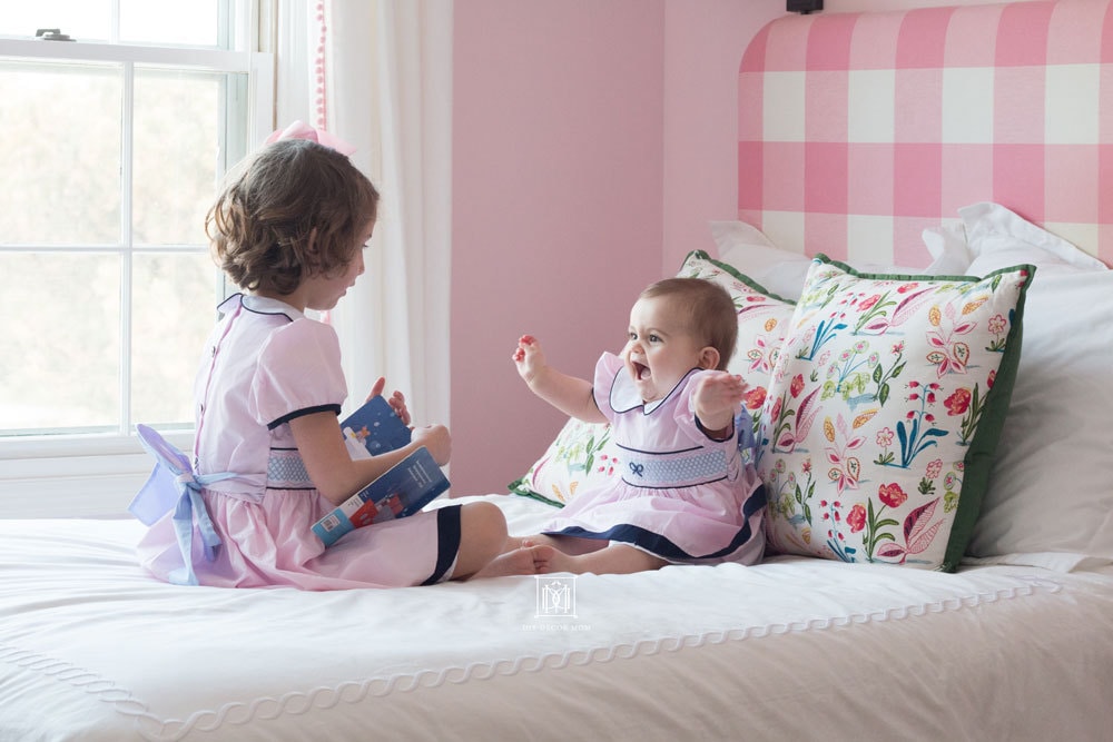 shared girls bedroom different ages baby and toddler on bed