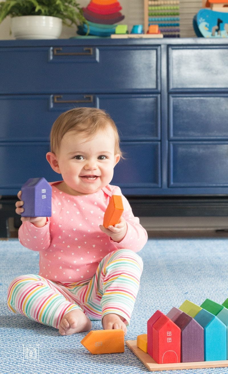 baby girl sitting on blue rug in playroom wearing baby clothes