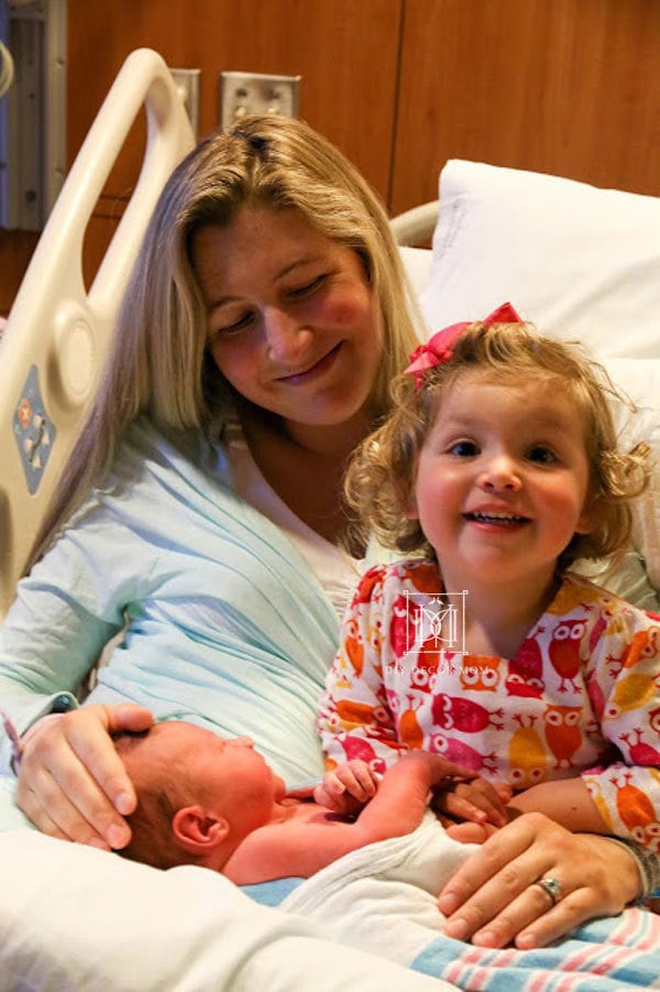 what to pack in diaper bag for hospital--picture of woman and newborn baby and toddler daughter at hospital after giving birth