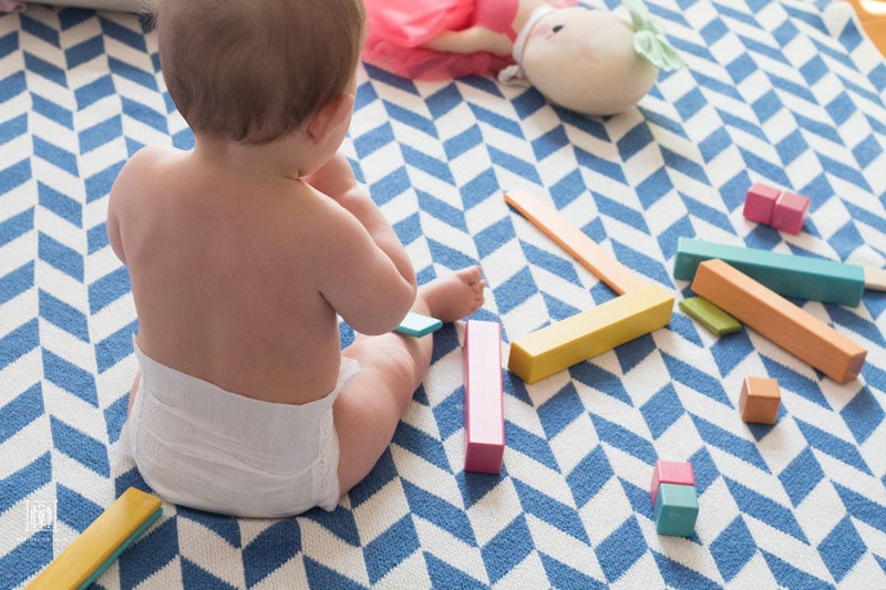 baby in diapers playing with wooden toys on blue and white blanket showcasing how to improve indoor air quality
