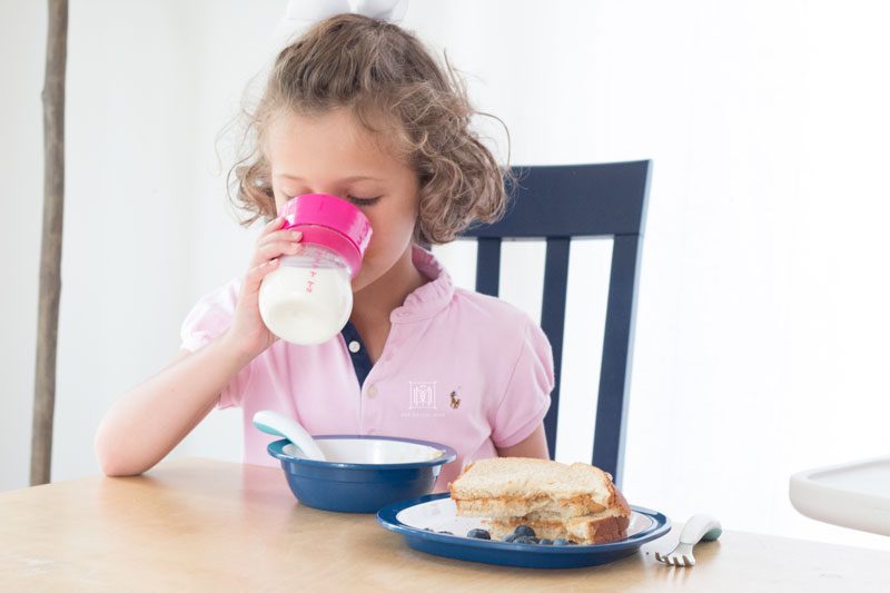 little girl drinking glass of milk from oxo transitions sippy cup