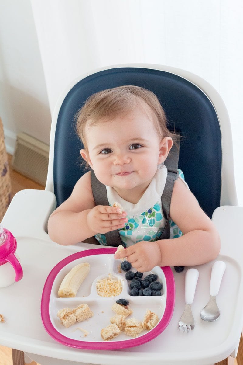 baby girl sitting in high chair with plate of baby led weaning food