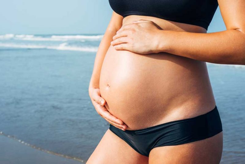 pregnant woman in bikini on beach things to do during your second trimester including taking a babymoon