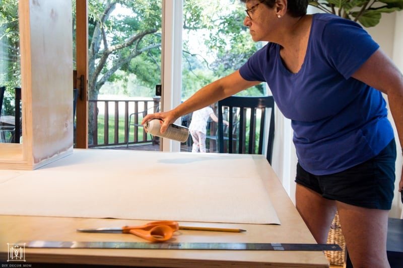 spraying spray adhesive to wrap a diy console table in fabric