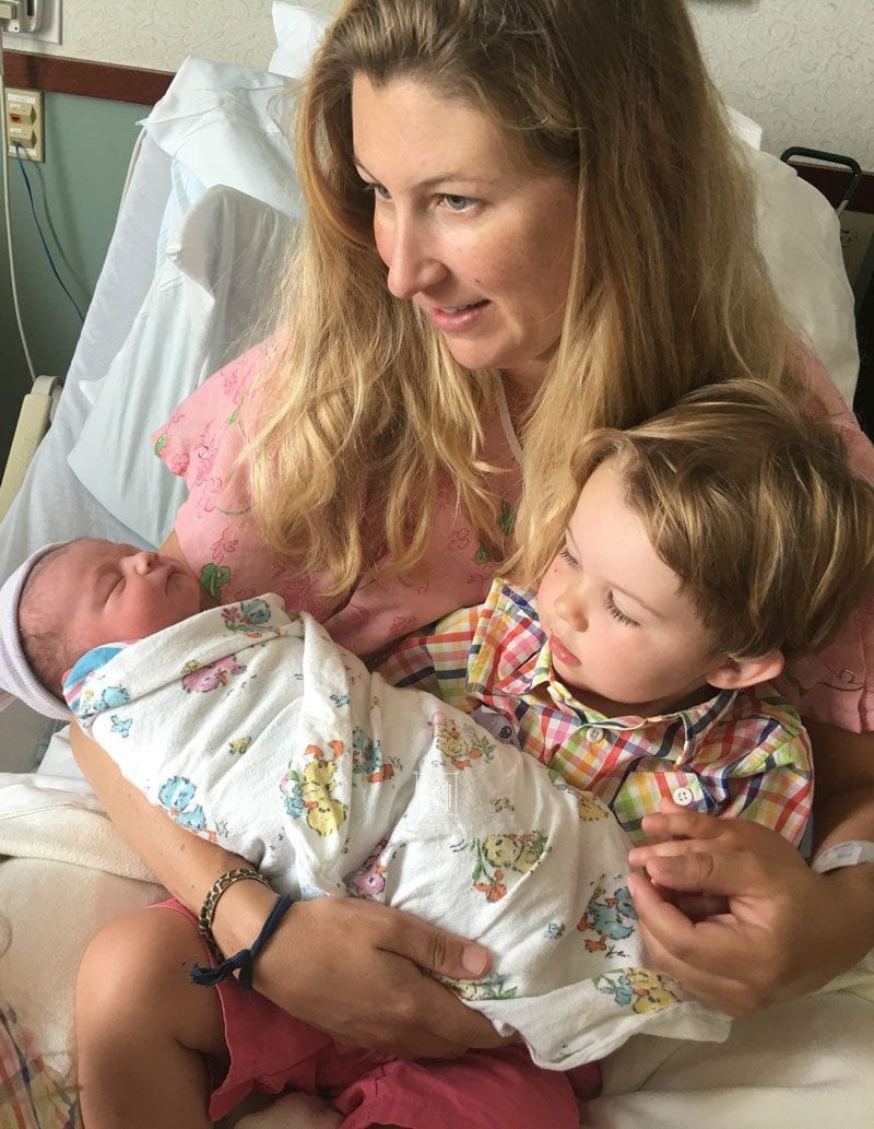 mom holds newborn baby and toddler son