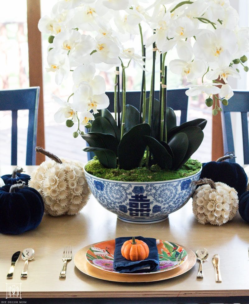 beautiful white orchids in blue and white ginger bowl with multicolored pumpkins of varying sizes including navy velvet pumpkins and white pumpkins