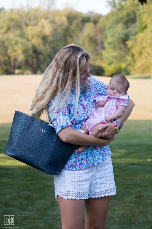 mom holding baby in backyard with blue diaper bag