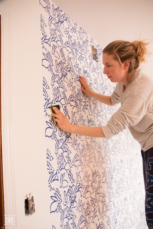 how to hang wallpaper: wmoan hanging wallpaper and wiping excess wallpaper adhesive off with wet sponge