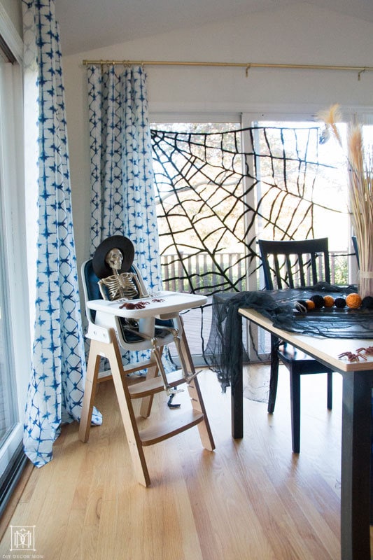 skeleton sitting in a high chair with giant spider web halloween table decor