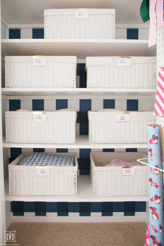 white baskets with bed sheets in a linen closet with blue and white wallpaper