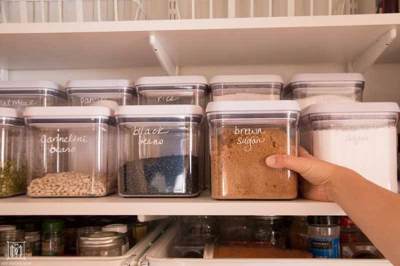person reaching for sugar in organized pantry with clear containers for baking ingredients