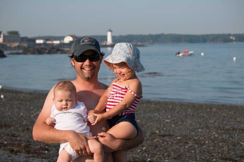 dad holds baby and toddler at beach--tips for helping toddler adjust to new baby