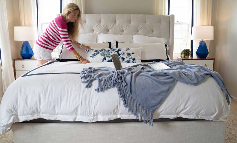 woman making bed with blue and white bedding