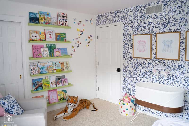 basinette and floating bookshelves in baby girl room with blue and white wallpaper
