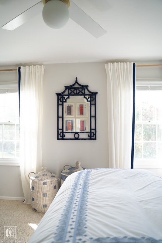 white curtains and white fan with gold touches in master bedroom with blue bamboo mirror and woven baskets