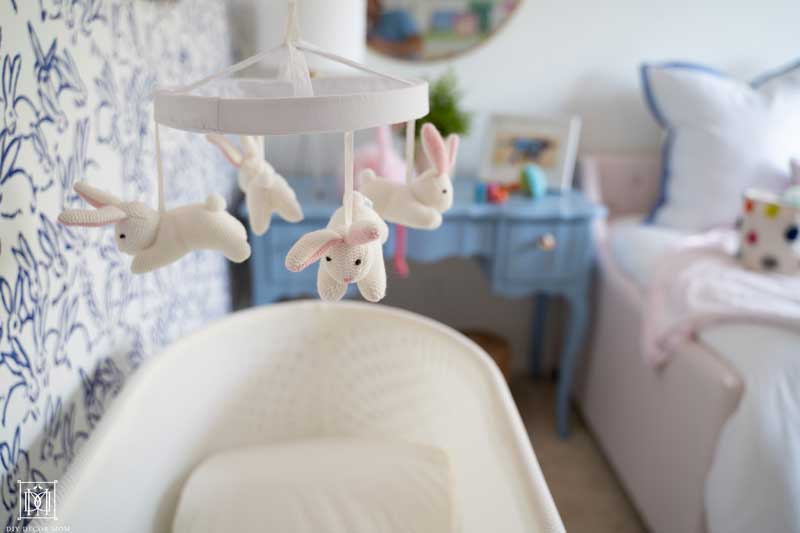 bunny mobile above snoo in baby girl nursery with blue nightstand and pink daybed