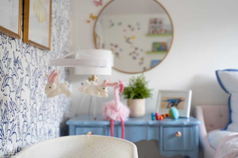 blue changing table with gold mirror and accent wallpaper in baby girl bedroom