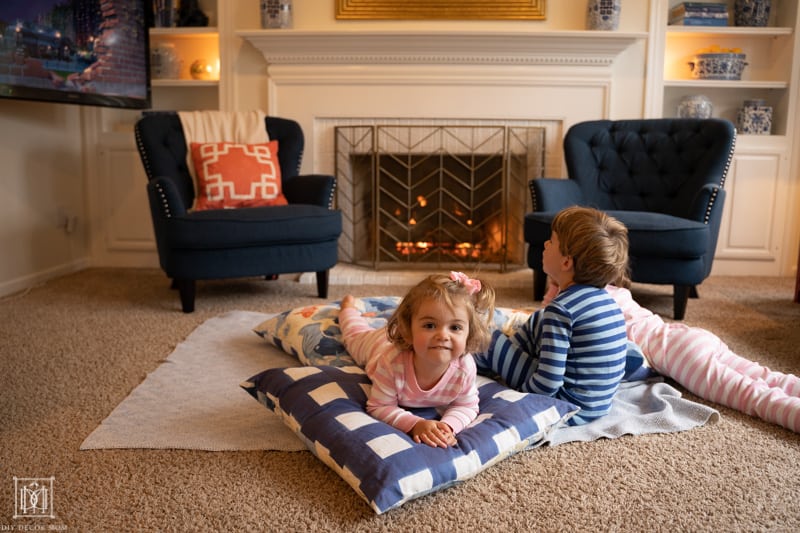 kids curled up in front of a fire watching a movie on floor pillows and a blanket--ways to increase your house hygge