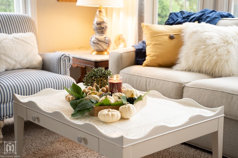 cozy picture of coffee table with candle burning on tray, warm lights, and soft furniture with fuzzy pillows--tips on making a cozy home