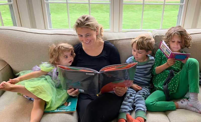 mom reading a book to her three kids on a couch