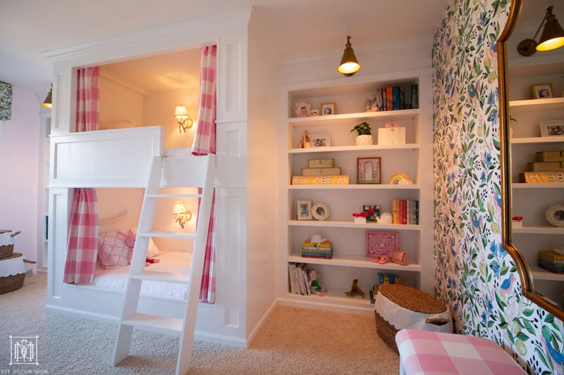 built-in bunk beds in girls bedroom with lights on and bookcase--beautiful shared girls pink and white and green bedroom