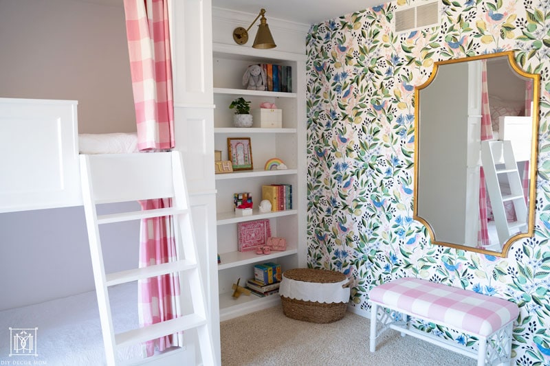 diy built-in bunk beds with curtains and white ladder in front of girls bedroom accent wall with wallpaper and gold and brass mirror and sconce