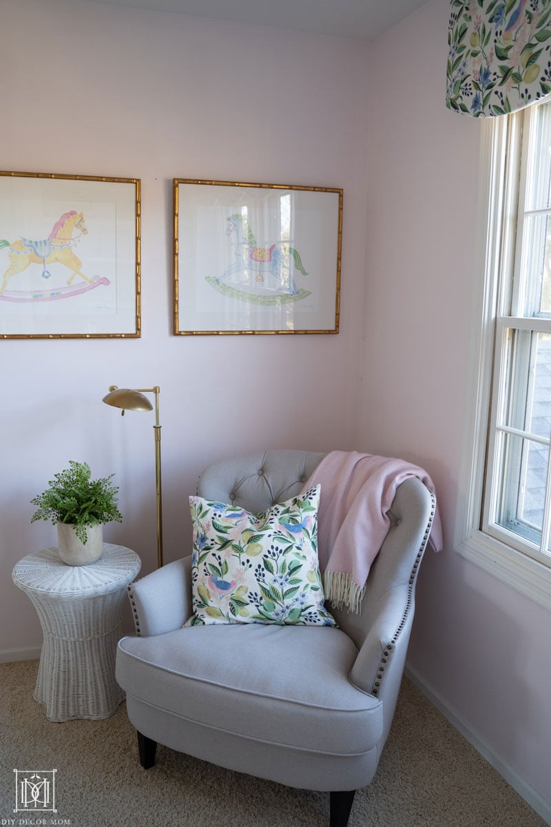 pale pink walls in shared girls bedroom with bunk beds- photo of a chair with a brass reading light and a white scalloped wicker side table with a green plant on top 