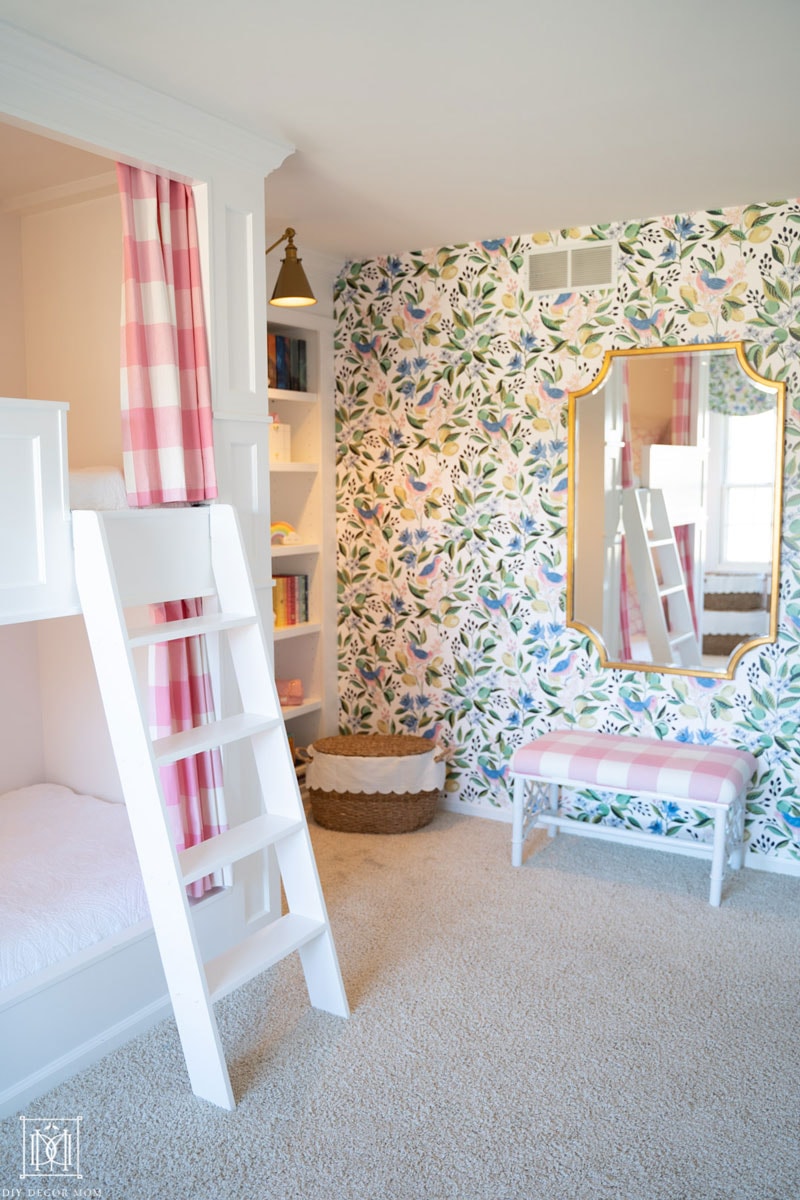 Built-in bunk beds with curtains and ladder in girls bedroom with preppy chinoiserie green and white wallpaper and beautiful gold mirror over a chinoiserie style bench covered in pink and white buffalo check. 