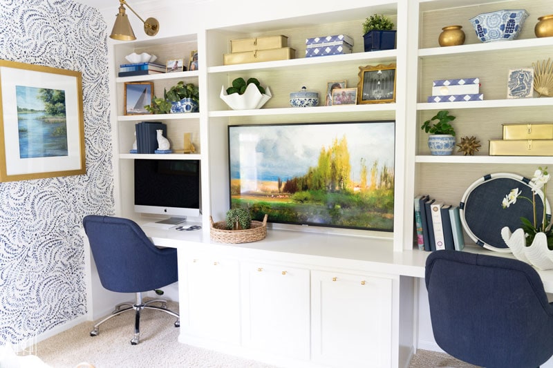 white diy built-in bookshelves and desk with grasscloth wallpaper and brass sconces with two work stations and TV in the middle