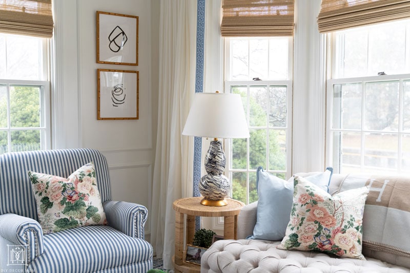 white living room with picture molding and tufted beige couch with chintz pillows and white and blue greek key trim curtains